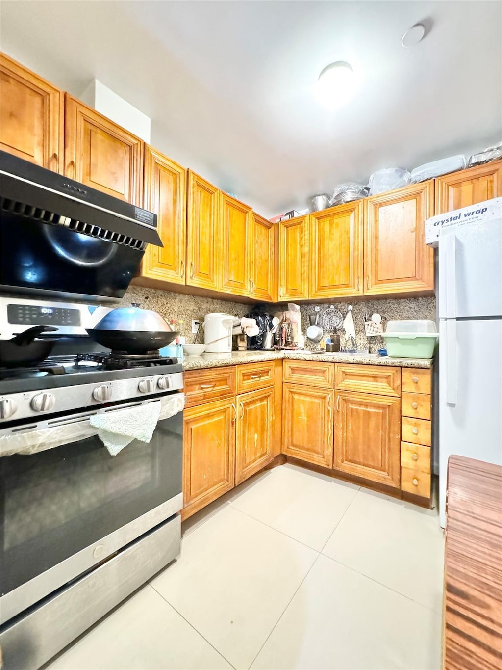 kitchen featuring freestanding refrigerator, exhaust hood, stainless steel gas range, light tile patterned flooring, and decorative backsplash