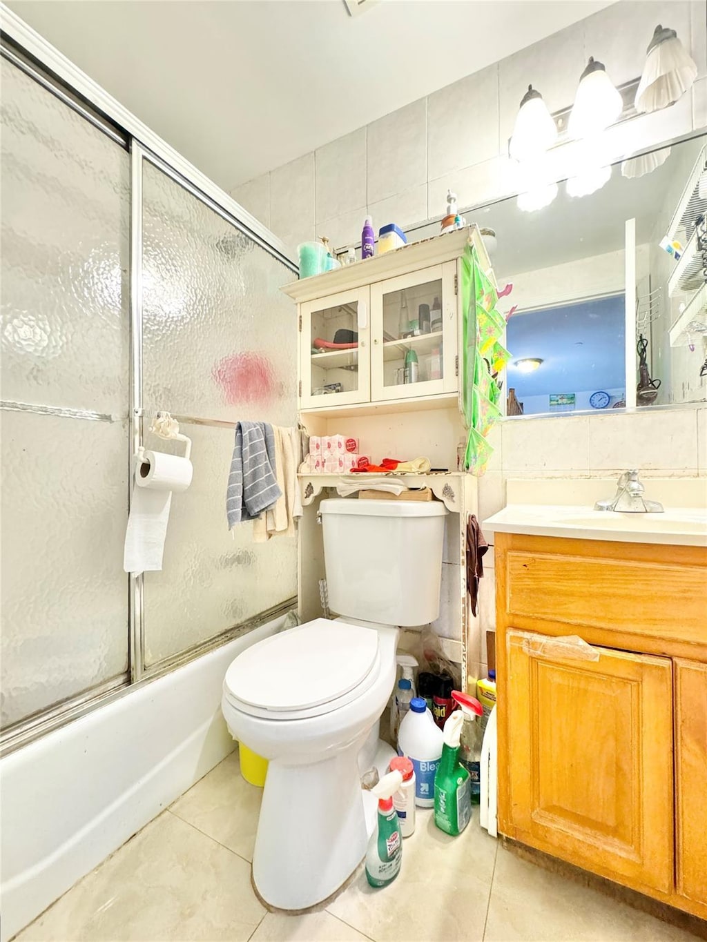 bathroom featuring tile patterned flooring, toilet, bath / shower combo with glass door, and vanity