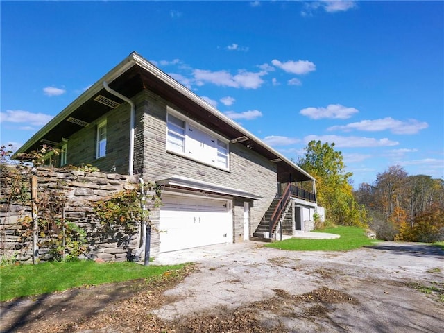 view of side of property with stairway, an attached garage, driveway, and stone siding