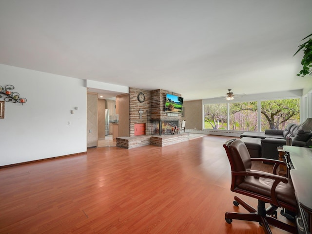 living room with a multi sided fireplace, a ceiling fan, wood finished floors, baseboards, and a baseboard radiator