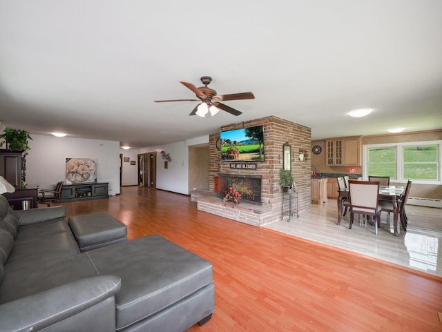 living area featuring light wood-style floors, a brick fireplace, ceiling fan, and baseboard heating