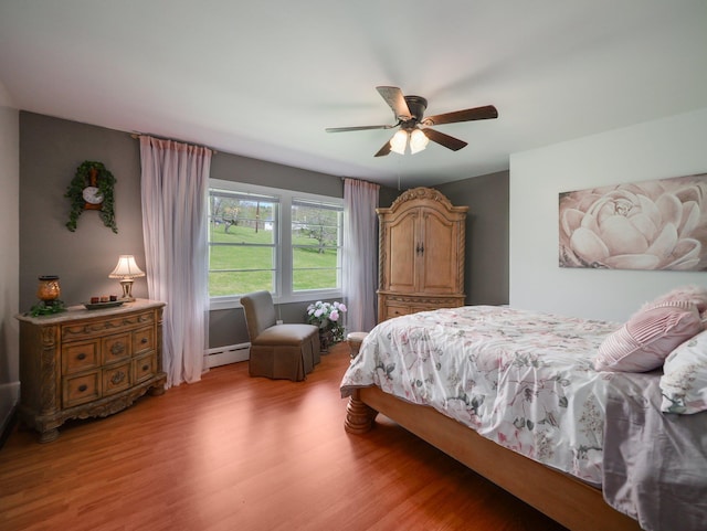 bedroom with a ceiling fan, light wood finished floors, and a baseboard heating unit