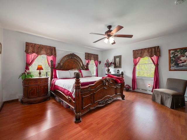 bedroom featuring light wood finished floors, ceiling fan, and a baseboard heating unit