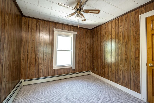 carpeted spare room with baseboard heating, a ceiling fan, and wood walls