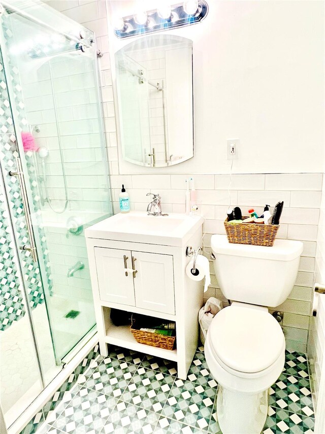 bathroom featuring a stall shower, tile patterned floors, tile walls, toilet, and wainscoting