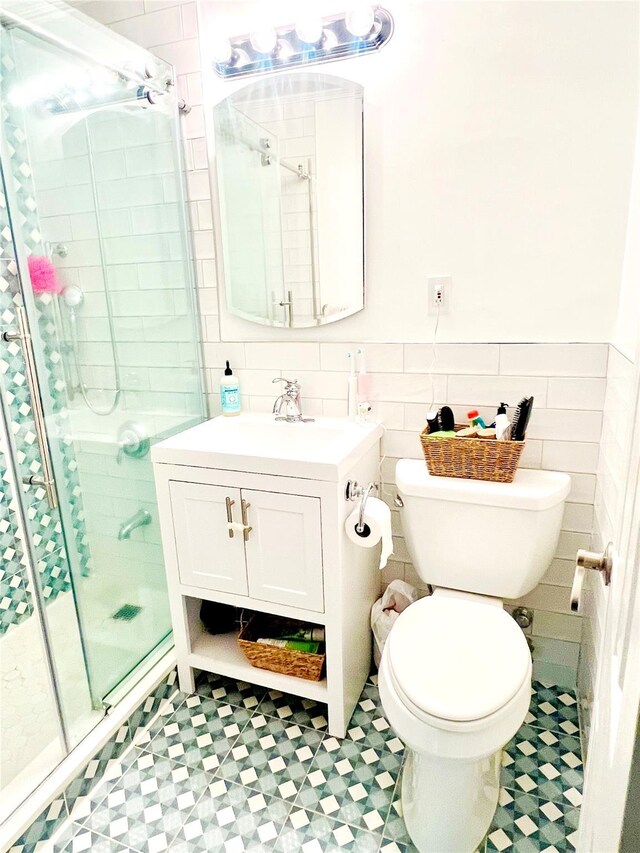 bathroom with a shower stall, toilet, tile patterned floors, a wainscoted wall, and tile walls