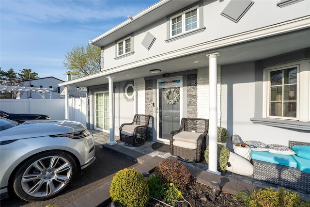 property entrance with a porch, fence, stone siding, and stucco siding