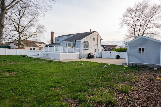 rear view of house featuring a deck, a patio, a fenced backyard, a chimney, and a lawn