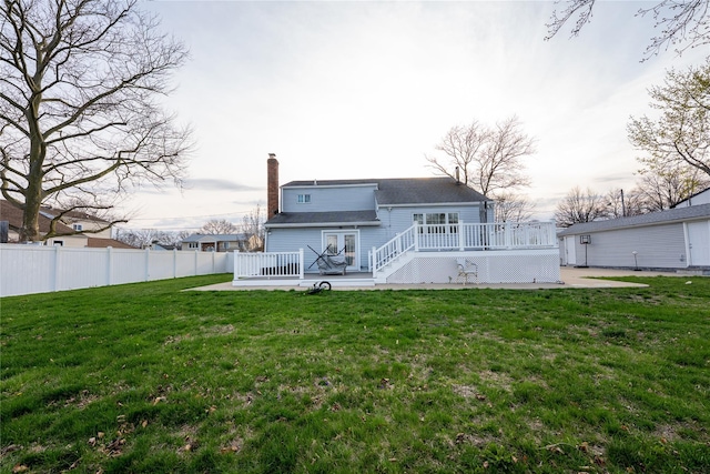 rear view of property with a lawn, a wooden deck, a chimney, and fence