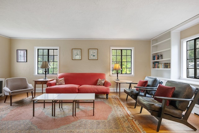 living area featuring wood finished floors, a textured ceiling, built in shelves, crown molding, and baseboards