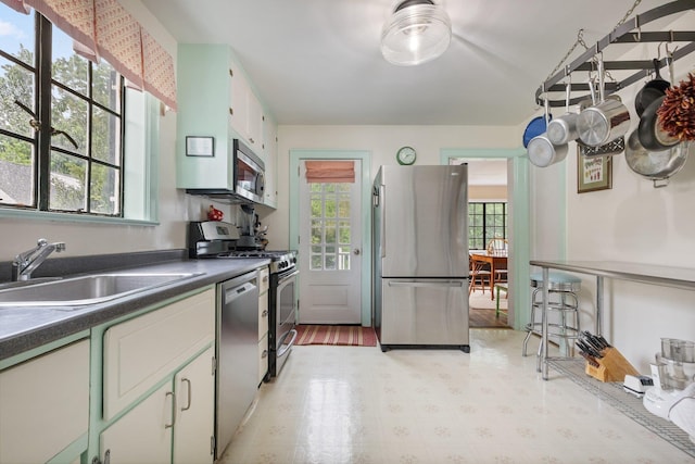 kitchen with a sink, light floors, dark countertops, and appliances with stainless steel finishes