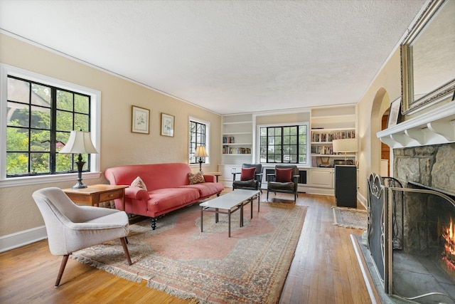 living area featuring hardwood / wood-style flooring, a textured ceiling, built in shelves, baseboards, and a stone fireplace