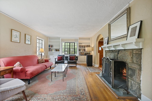 living room featuring a textured ceiling, a stone fireplace, built in features, arched walkways, and light wood-type flooring