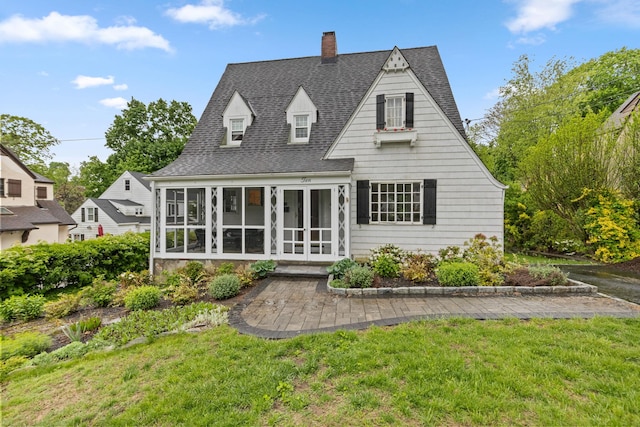 back of house featuring a sunroom, a chimney, a shingled roof, a yard, and french doors