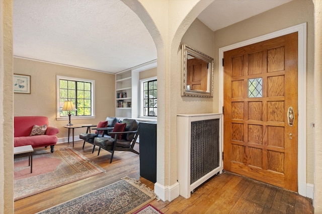 foyer featuring arched walkways, hardwood / wood-style floors, and baseboards