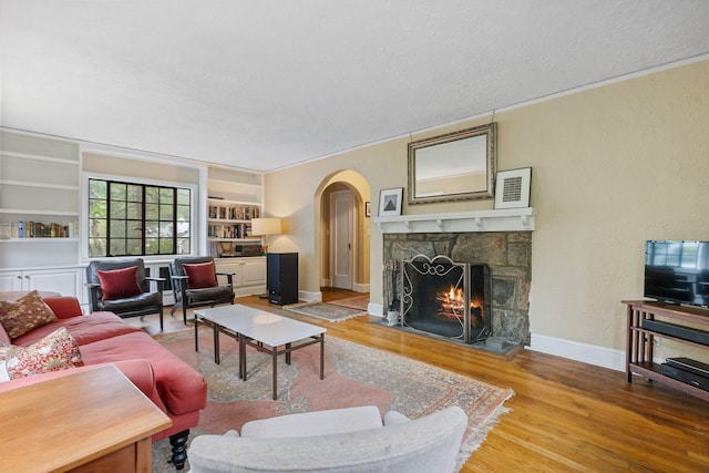 living area featuring wood finished floors, a textured wall, arched walkways, baseboards, and a stone fireplace