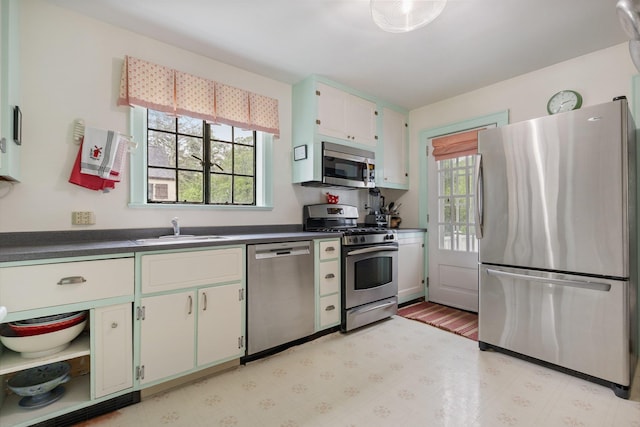 kitchen featuring a sink, light floors, white cabinetry, dark countertops, and appliances with stainless steel finishes