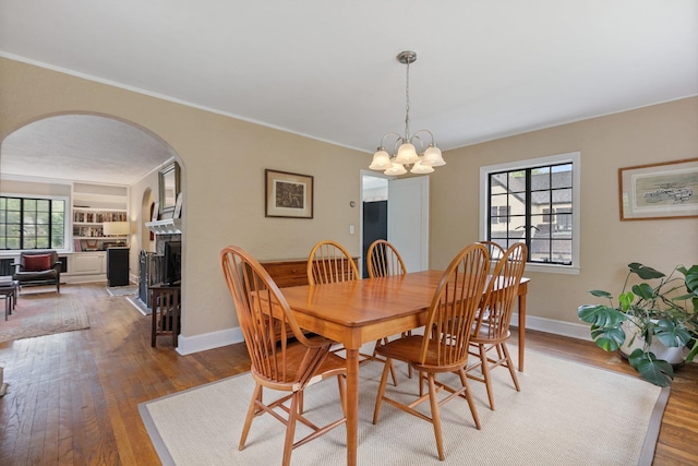dining space featuring baseboards, a chandelier, wood finished floors, arched walkways, and a fireplace