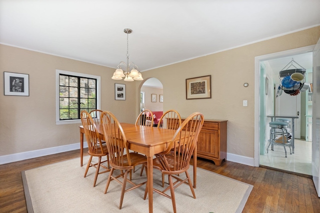 dining room featuring a notable chandelier, baseboards, arched walkways, ornamental molding, and dark wood-style floors