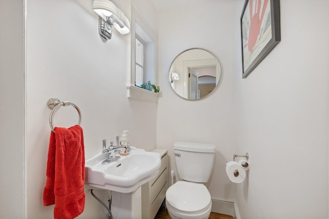 half bathroom featuring toilet, wood finished floors, and a sink