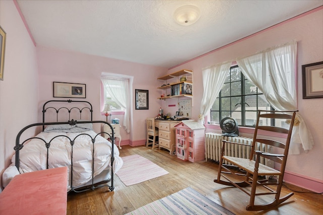 bedroom with radiator, baseboards, light wood-type flooring, and multiple windows