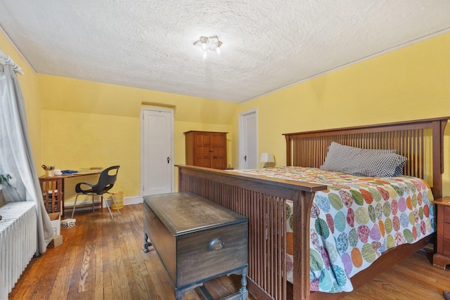 bedroom featuring wood-type flooring, a textured ceiling, baseboards, and radiator heating unit