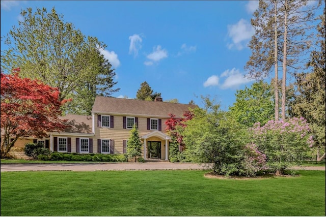 colonial inspired home featuring a chimney and a front yard