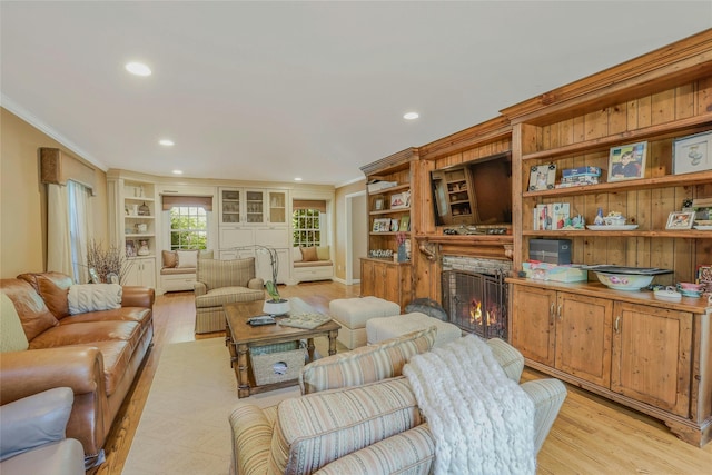 living area with crown molding, recessed lighting, light wood-style floors, and a warm lit fireplace
