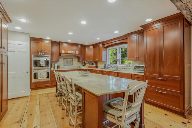 kitchen with brown cabinetry, double oven, light wood-style floors, a breakfast bar area, and a center island