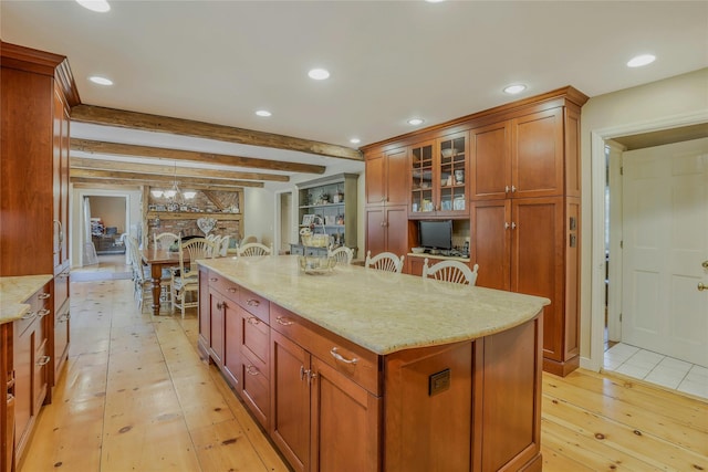 kitchen with brown cabinetry, beam ceiling, glass insert cabinets, light wood-type flooring, and light stone counters