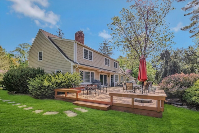back of property featuring a yard, a deck, a chimney, and outdoor dining space