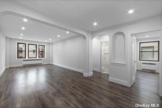 34-24 82nd St Unit 6E, Jackson Heights, NY 11372 - unfurnished living room featuring radiator heating unit, arched walkways, baseboards, dark wood finished floors, and recessed lighting