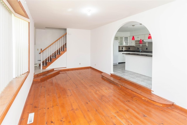 57 E Rock Cut Rd, Walden, NY 12586 - unfurnished living room featuring arched walkways, stairs, baseboards, light wood-type flooring, and baseboard heating