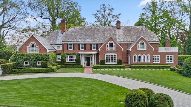 view of front of house featuring a chimney, a front lawn, a high end roof, and brick siding