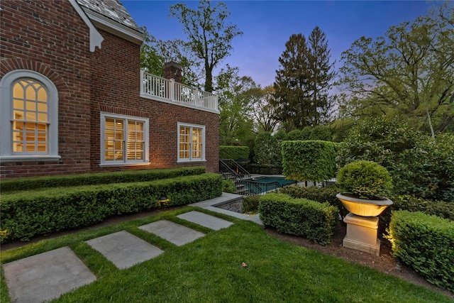 yard at dusk with a balcony and a lawn