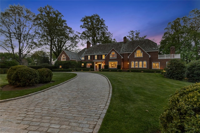 colonial home featuring a front yard, curved driveway, a chimney, and brick siding
