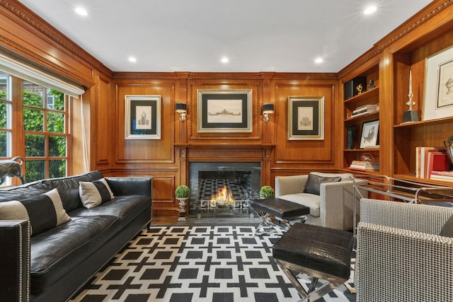living area with a lit fireplace, ornamental molding, recessed lighting, a decorative wall, and built in features