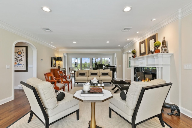 living area with a glass covered fireplace, wood finished floors, recessed lighting, crown molding, and baseboards