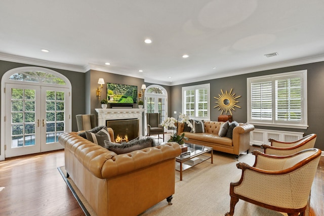 living area with french doors, recessed lighting, wood finished floors, healthy amount of natural light, and a warm lit fireplace