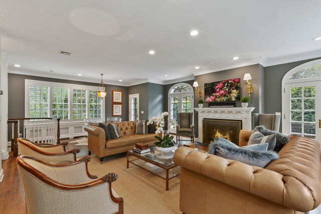 living room featuring recessed lighting, plenty of natural light, a warm lit fireplace, wood finished floors, and ornamental molding