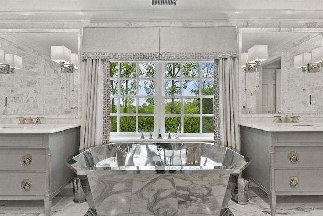 bathroom with two vanities, marble look tiles, and a freestanding tub