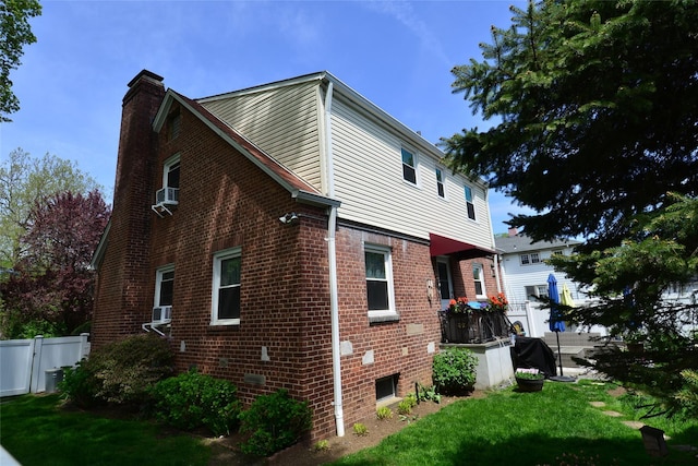 view of home's exterior with fence, cooling unit, a chimney, brick siding, and a yard