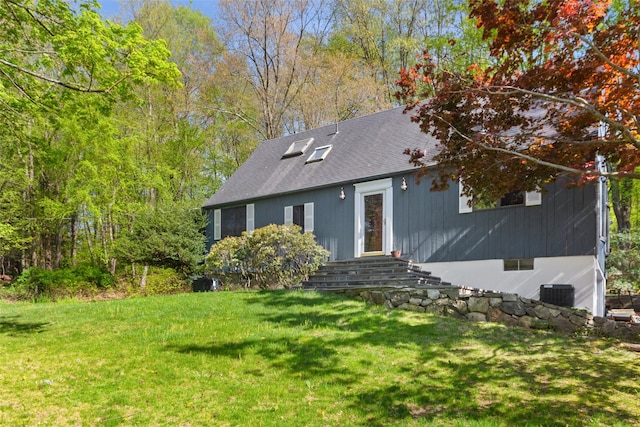view of front of house with a front yard, a shingled roof, and central AC unit