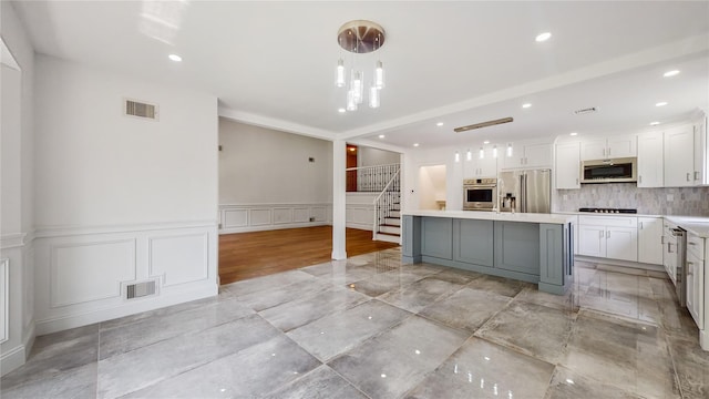 kitchen featuring stainless steel appliances, a decorative wall, light countertops, a kitchen island with sink, and white cabinets