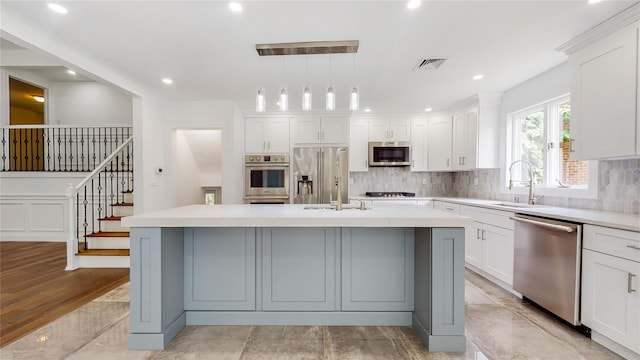 kitchen with stainless steel appliances, a sink, decorative backsplash, a kitchen island with sink, and light countertops