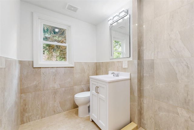 bathroom featuring tile walls, toilet, vanity, and wainscoting