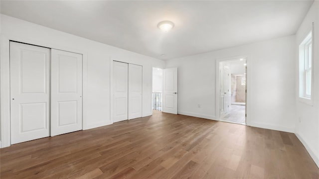 unfurnished bedroom featuring multiple closets, wood finished floors, baseboards, and ensuite bath