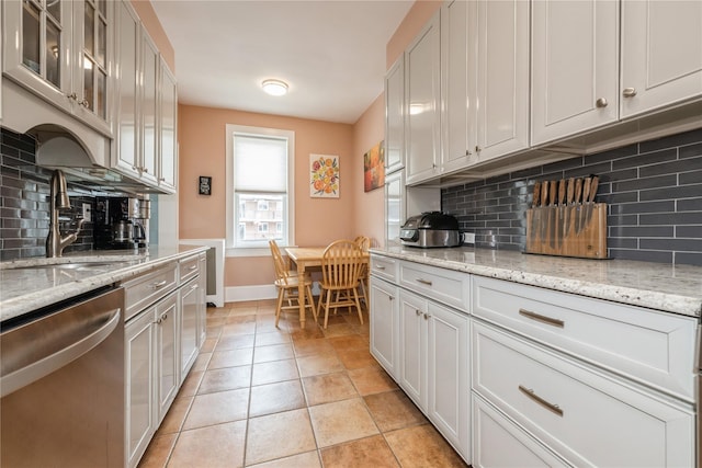 kitchen with glass insert cabinets, a sink, baseboards, dishwasher, and tasteful backsplash