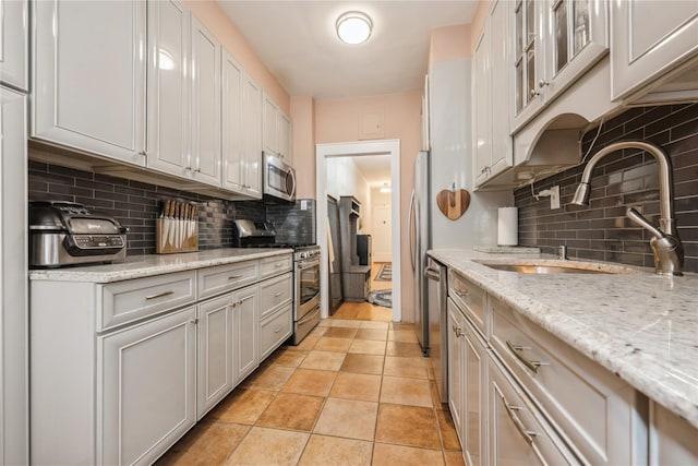 kitchen featuring a sink, light stone countertops, backsplash, and appliances with stainless steel finishes