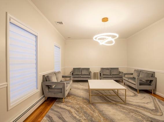 10-12 Damian Ct, Chester, NY 10918 - living room featuring a baseboard radiator, a chandelier, wood finished floors, and crown molding